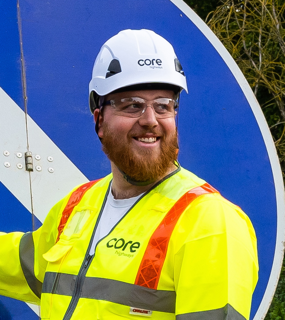 Core highways team member smiling in front of traffic sign