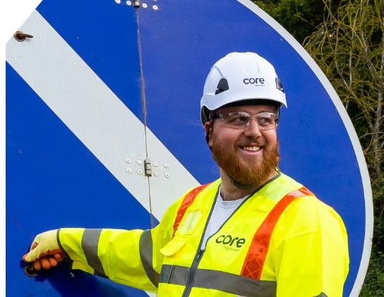 Core highways worker smiling in front of road sign